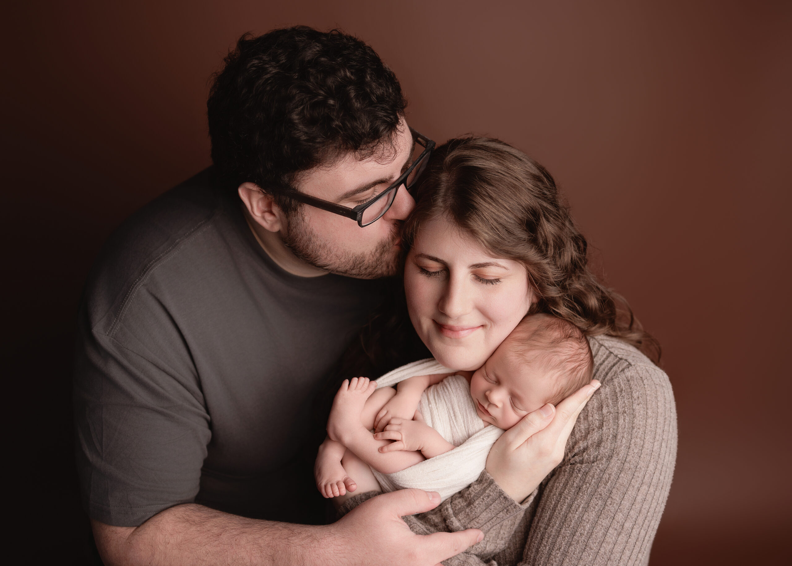 Family of 3 posed in front of a photo backdrop for newborn photos in Grants Pass